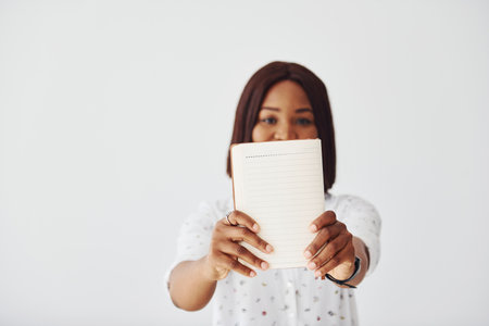 Young african american woman in formal clothes standing with notepad and empty paper in hands indoorsの写真素材