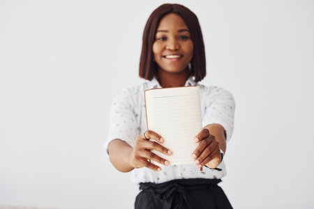 Young african american woman in formal clothes standing with notepad and empty paper in hands indoorsの写真素材