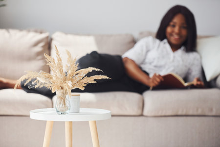Positive african american woman in white shirt lying down on sofa with notepad in handsの写真素材
