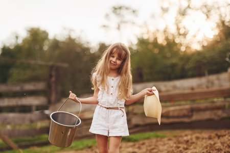Little girl in white clothes is on the farm at summertime outdoors with milkの写真素材