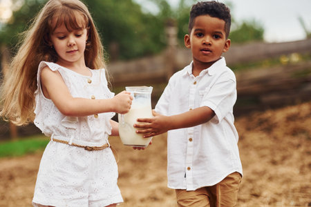 Cute little african american boy with european girl is on the farm with milkの写真素材