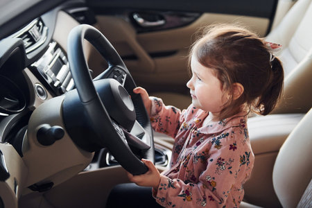 Cute little girl sitting on the drivers seat inside of modern carの写真素材