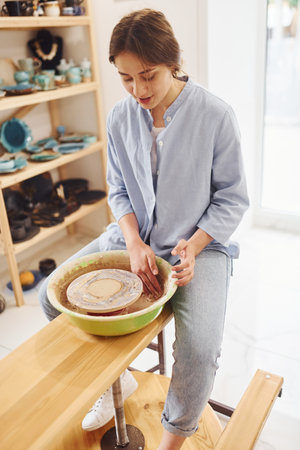 Young female ceramist working by using pottery wheel indoors and making handmade clay productの写真素材