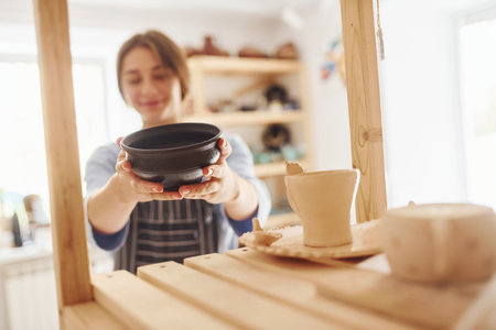 Job is done. Young female ceramist indoors with finished handmade clay product. Conception of potteryの写真素材