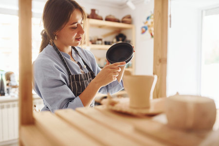 Job is done. Young female ceramist indoors with finished handmade clay product. Conception of...