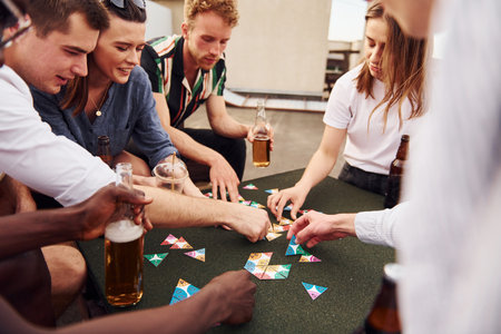 Playing card game. Group of young people in casual clothes have a party at rooftop together at daytimeの写真素材