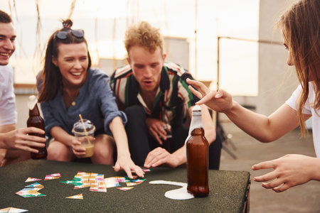 Playing card game. Group of young people in casual clothes have a party at rooftop together at daytimeの写真素材