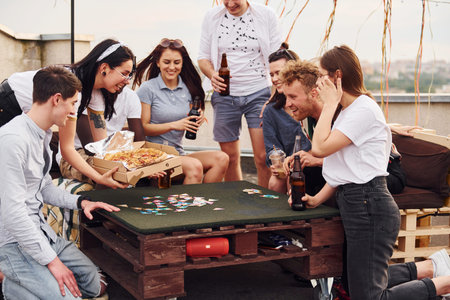 With delicious pizza. Group of young people in casual clothes have a party at rooftop together at...
