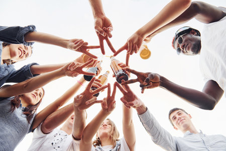 Making beautiful gesture by fingers. View from below. Group of young people in casual clothes have a party at rooftop together at daytimeの写真素材