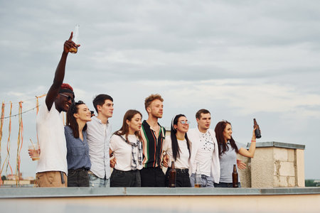 Decorated place. Cloudy weather. Group of young people in casual clothes have a party at rooftop together at daytimeの写真素材