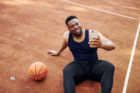 Making selfie. African american man plays basketball on the court outdoorsの写真素材