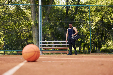 Beautiful green trees on background. African american man plays basketball on the court outdoors