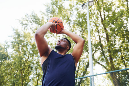 Cloudy weather. African american man plays basketball on the court outdoorsの写真素材