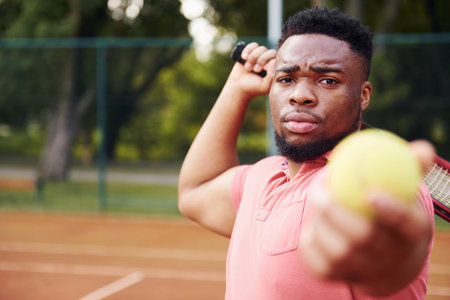African american man in pink shirt plays tennis on the court outdoorsの写真素材