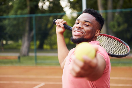 African american man in pink shirt plays tennis on the court outdoorsの写真素材