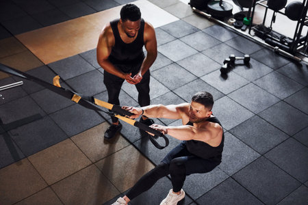 Personal trainer is on job. African american man with white guy have workout day in gymの写真素材