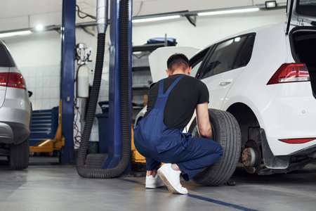 Man in work uniform repairs car indoors. Conception of automobile serviceの写真素材