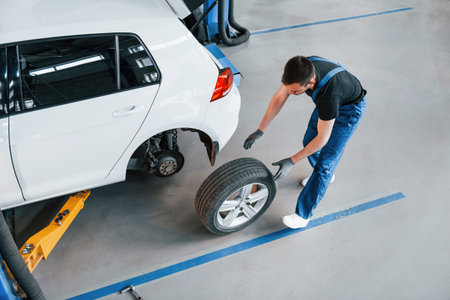 Top view. Man in work uniform walking with car wheel indoors. Conception of automobile serviceの写真素材