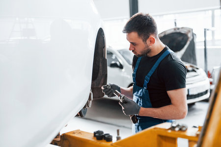 Man in work uniform repairs car indoors. Conception of automobile serviceの写真素材