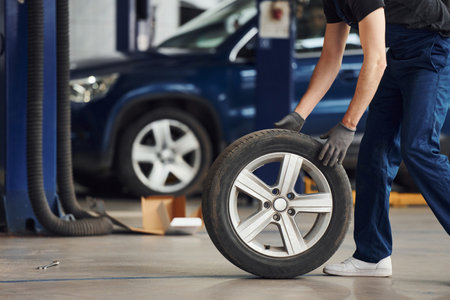 Close up view of man in work uniform with car wheel indoors. Conception of automobile serviceの写真素材