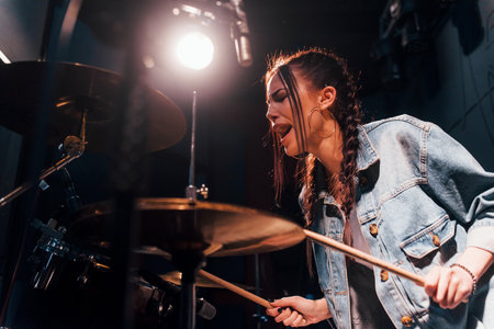 Plays drums. Young beautiful female performer rehearsing in a recording studioの写真素材