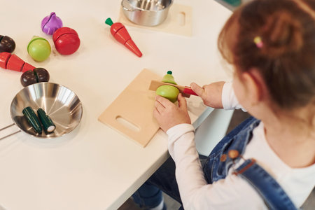 Little girl in casual clothes sits by table and having fun by playing with toys on the kitchenの写真素材