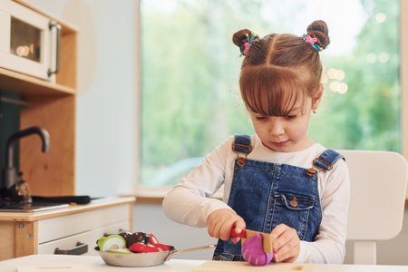 Little girl in casual clothes sits by table and having fun by playing with toys on the kitchenの写真素材