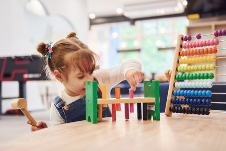 Cheerful little girl in casual clothes playing in kindergarten with toysの写真素材
