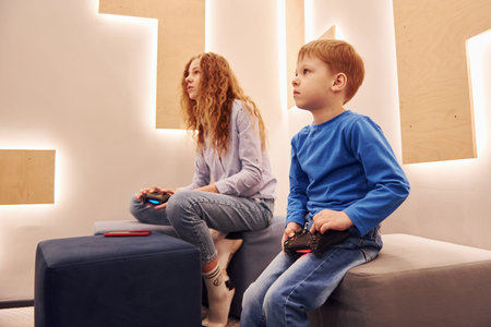Cheerful kids sitting indoors and playing video games together
