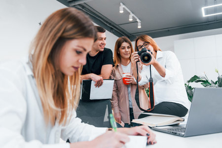 Woman making photo by camera. Group of business people in formal clothes indoors in the officeの写真素材