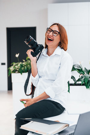 Woman in formal clothes and with camera sitting in the officeの写真素材