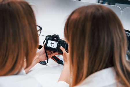 Two women sitting by the table and looking at photos that is in cameraの写真素材