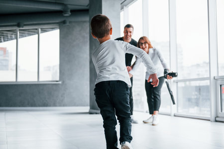 Woman in formal clothes and with camera in hand standing inside of empty room with man and little boy that running and having funの写真素材
