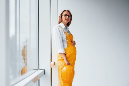 Female worker or engineer in yellow uniform and hard hat standing indoorsの写真素材