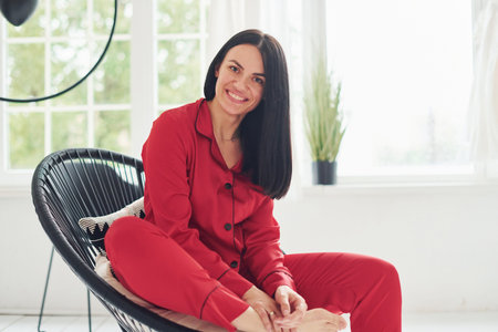 Cheerful young woman in pajamas sitting on the chair indoors at daytime