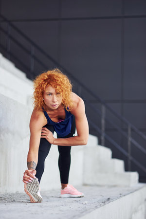 Young european redhead woman in sportive clothes doing exercises on stairs outdoorsの写真素材
