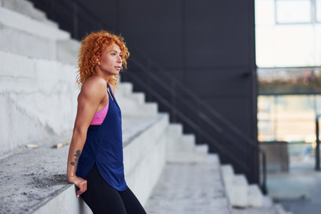 Young european redhead woman in sportive clothes standing on stairs outdoorsの写真素材