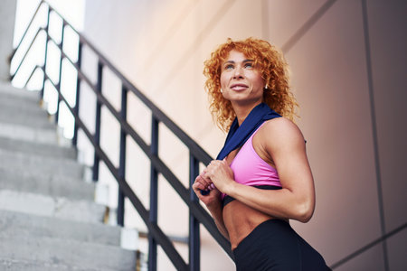 Young european redhead woman in sportive clothes showing her body and posing outdoors after fitness exercisesの写真素材