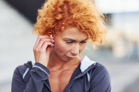 Listening to the music in headphones. Portrait of young european redhead woman that standing outdoorsの写真素材