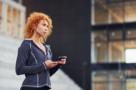 Portrait of young european redhead woman that standing with phone in hands outdoors