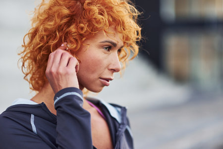 Listening to the music in headphones. Portrait of young european redhead woman that standing outdoorsの写真素材