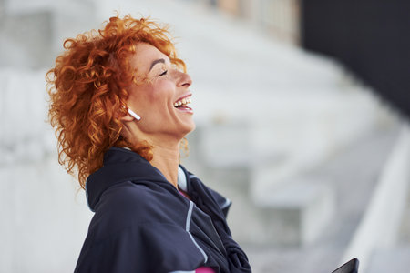 Young european redhead woman in sportive clothes standing on stairs outdoors with phone in handsの写真素材