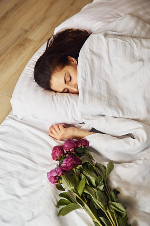 Lying down on bed with flowers. Young woman resting and spending weekend at home alone at homeの写真素材