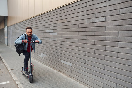 Side view of handsome young guy in casual clothes that riding electric schooter outdoors at sunny daytimeの写真素材