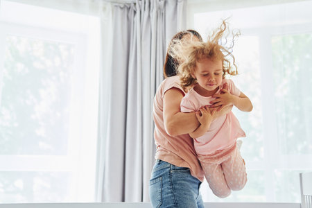 Playing with each other at weekend time. Young mother with her little daughter in casual clothes together indoors at homeの写真素材