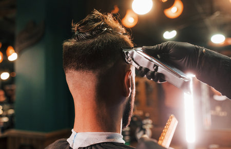 Close up view of young bearded man that sitting and getting haircut in barber shopの写真素材