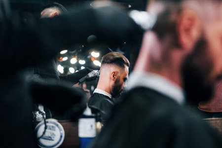 Young bearded man sitting and getting haircut in barber shopの写真素材