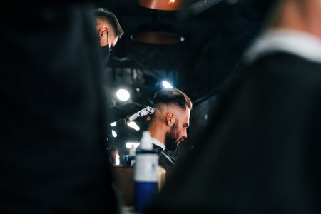 Young bearded man sitting and getting haircut in barber shopの写真素材