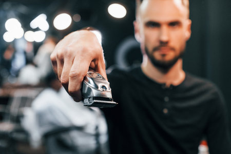Young bearded man standing in barber shop and holding clipperの写真素材