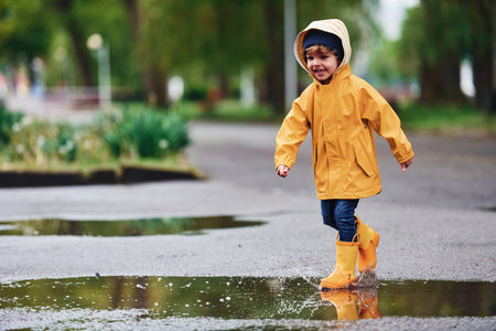 Kid in yellow waterproof cloak and boots playing outdoors after the rainの写真素材